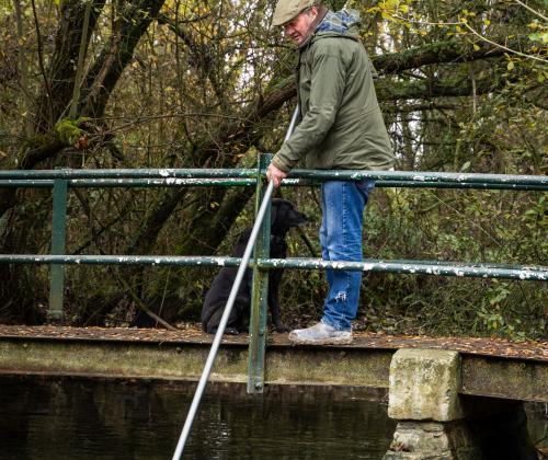 a man stands on a bridge over a river holding a pole into the river